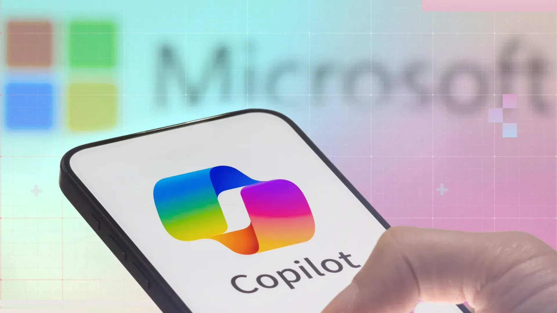 Hand holding a phone displaying the Microsoft Copilot logo with the Microsoft logo blurred in the background.
