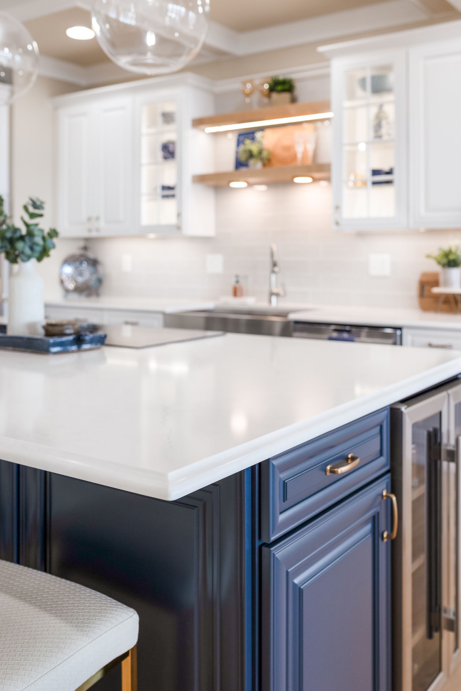 Calacatta Miraggio Cielo Q Quartz Countertops, Armonie Picadilly Avorio Glossy Tile Backsplash, Waypoint Painted Linen Perimeter Cabinets, Painted Navy Island Cabinets, and Maple Rye Floating Shelves