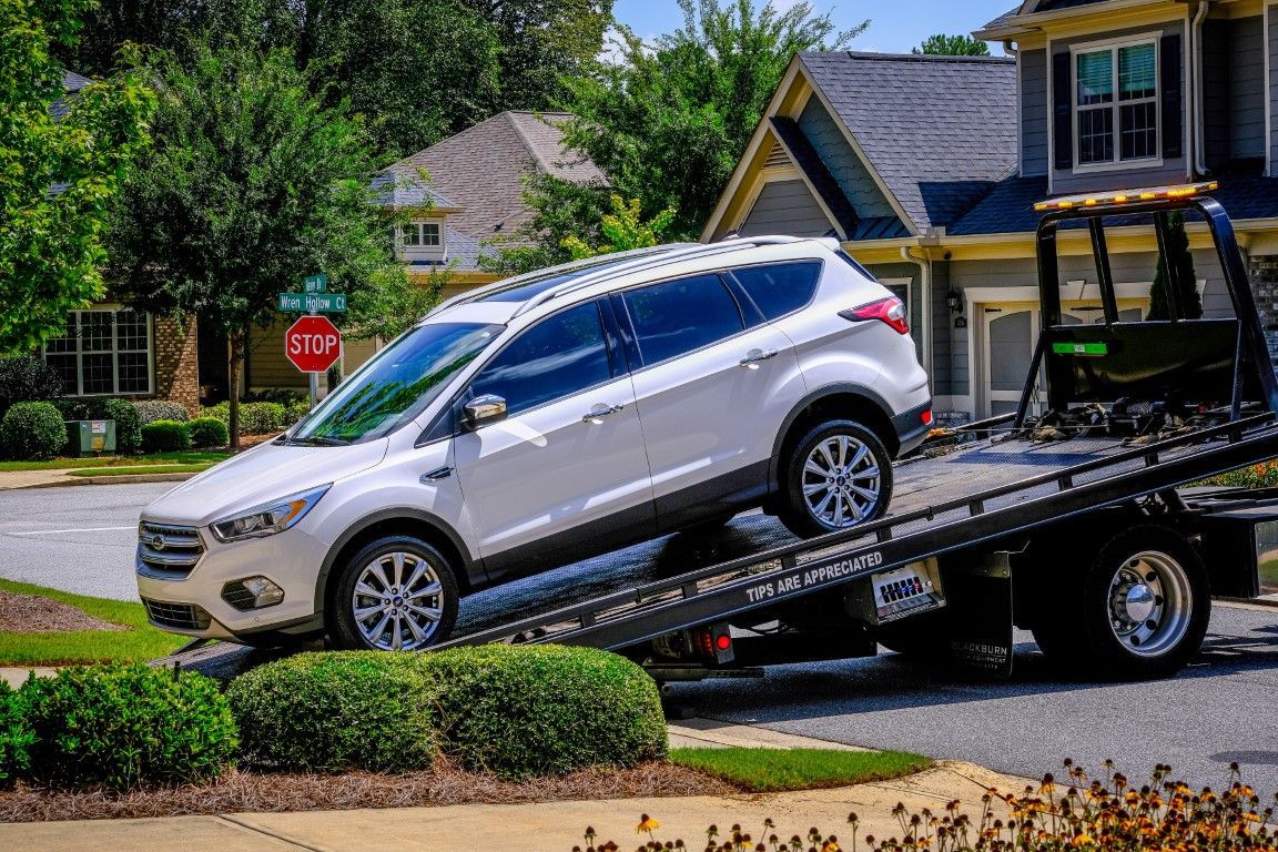 White SUV being towed onto a flatbed tow truck in a residential area.