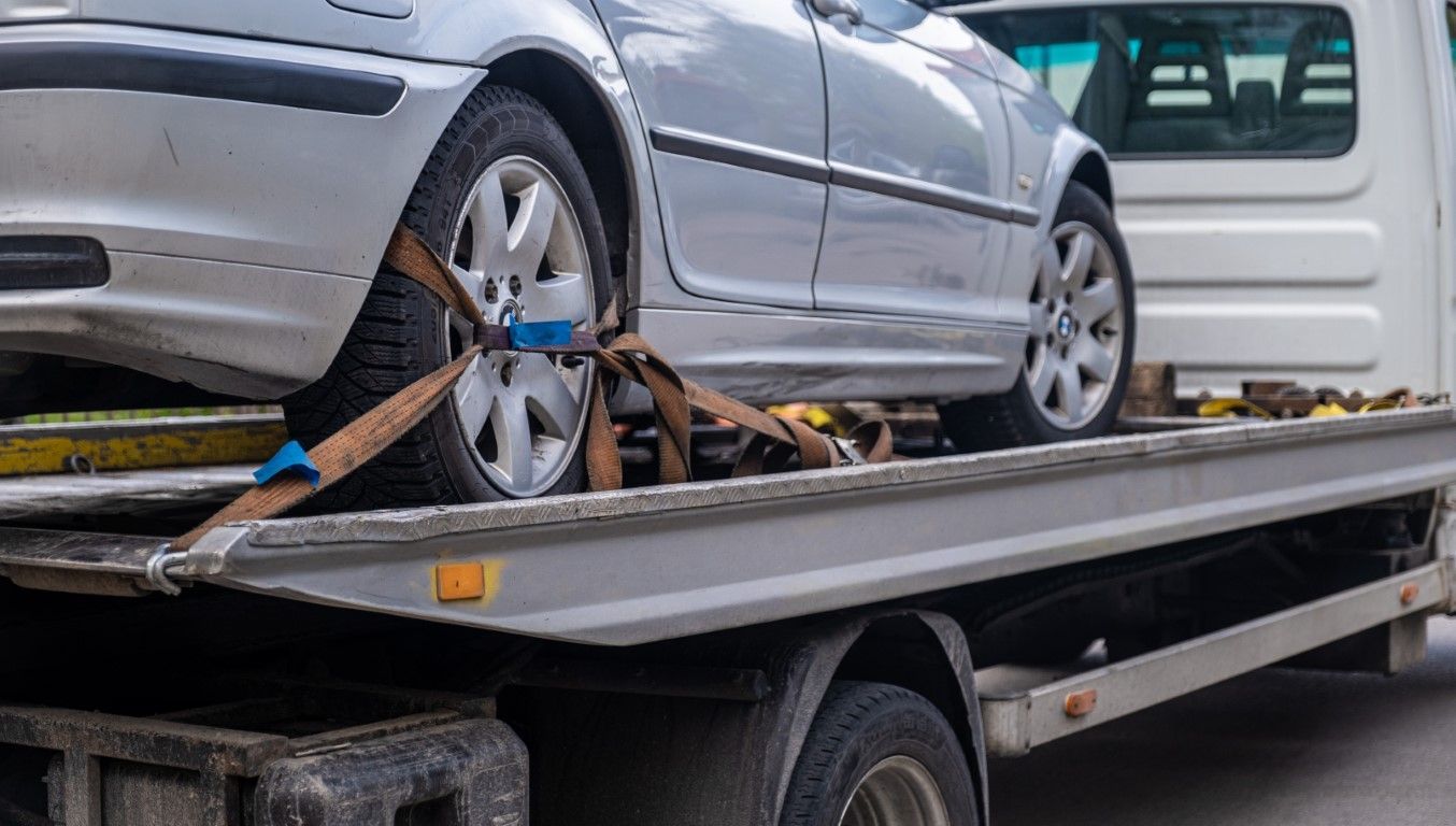 Silver car secured on a flatbed tow truck for transport.