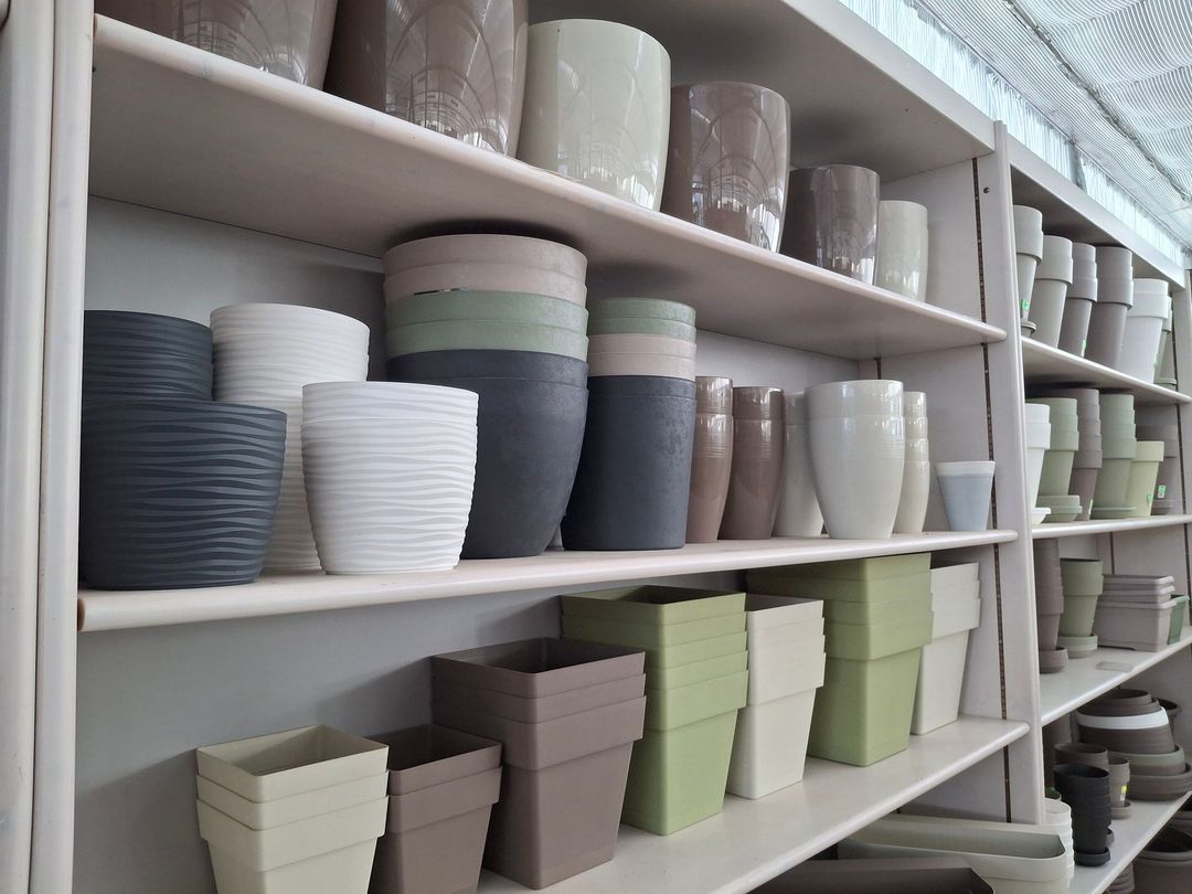 Scaffali pieni di vari vasi di ceramica nelle tonalità del grigio, del beige e del verde, esposti in un ambiente da negozio.