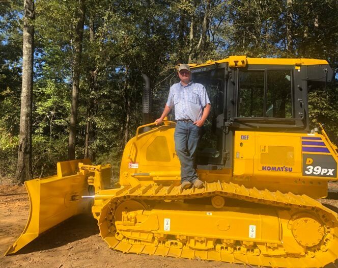 A man is standing on top of a yellow bulldozer.