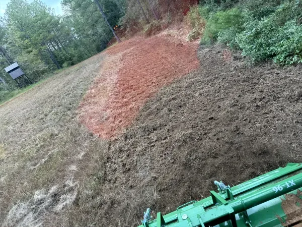 A green tractor is plowing a dirt field.