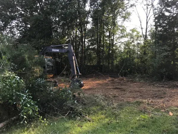 A large excavator is sitting in the middle of a field surrounded by trees.