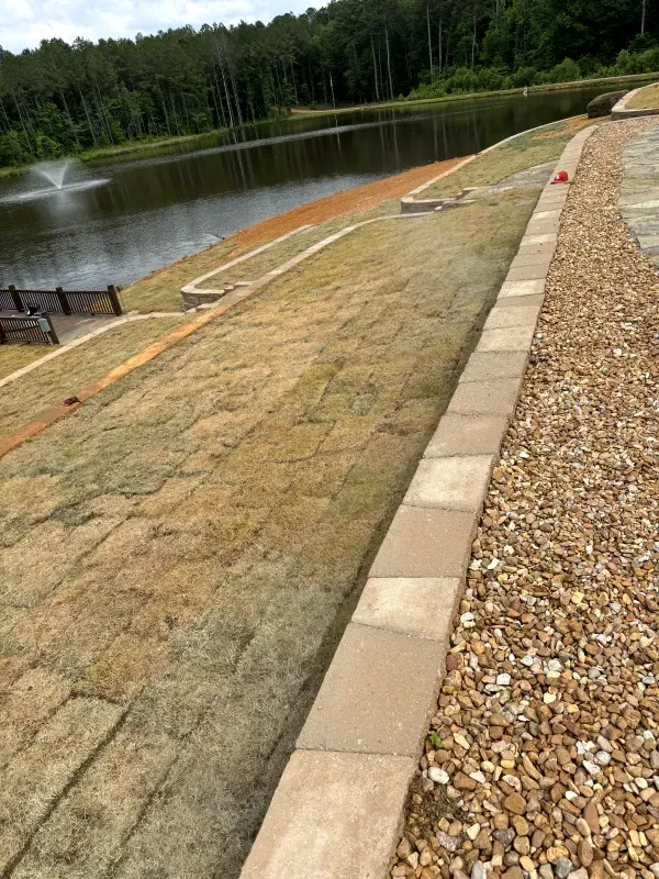 A brick walkway leading to a lake with a fountain in the background.