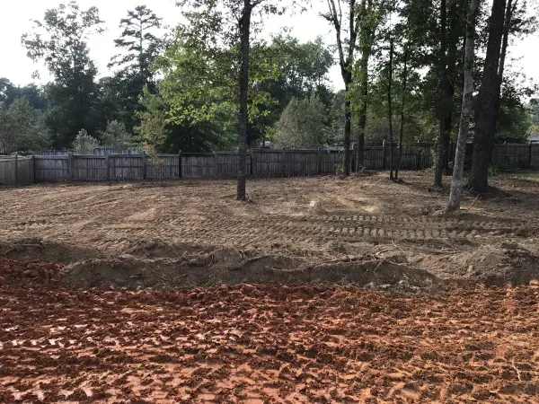 A dirt field with a fence and trees in the background.