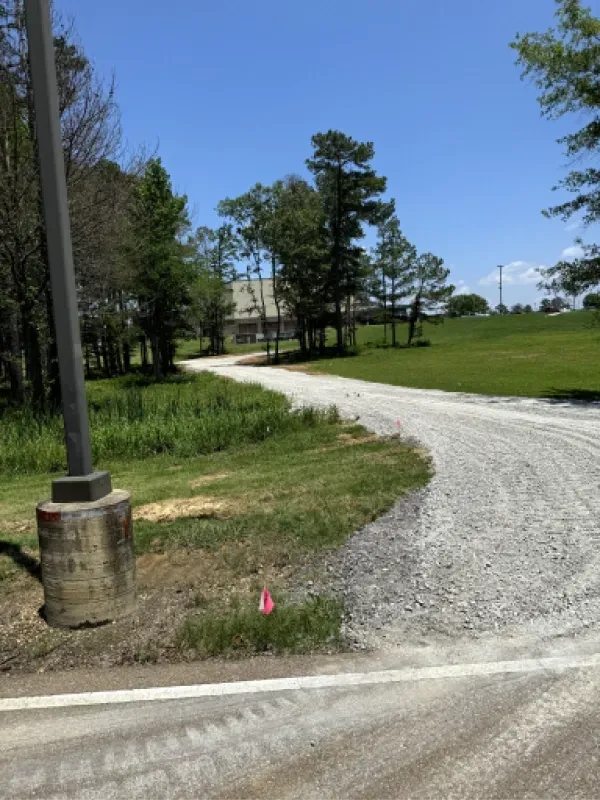A dirt road going through a grassy field with a house in the background.