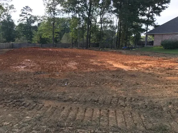A dirt field with a house in the background and trees in the background.
