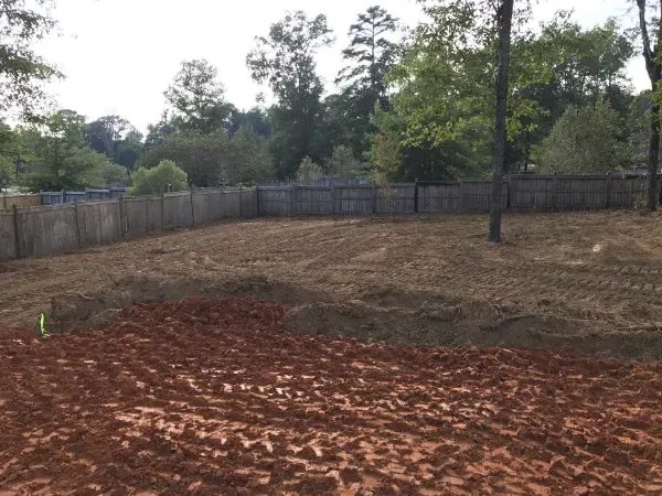 A dirt field with a fence and trees in the background.