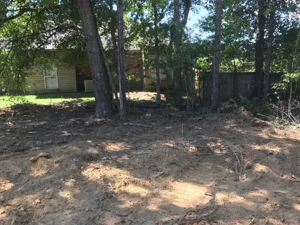 A dirt field with trees in the background and a house in the background.