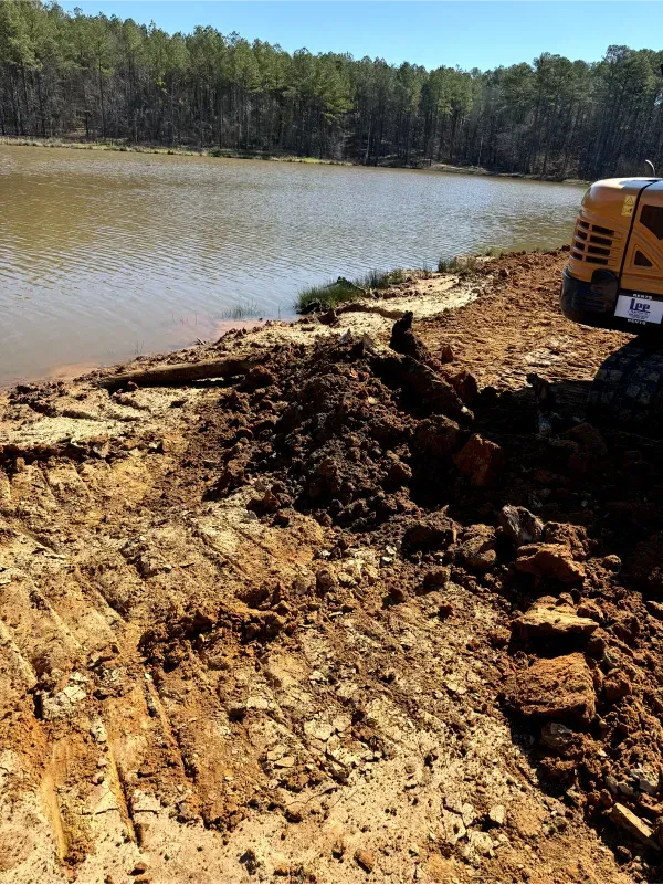 A yellow excavator is digging in the dirt near a lake