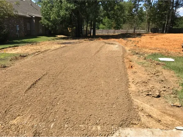 A dirt road leading to a house with trees in the background.