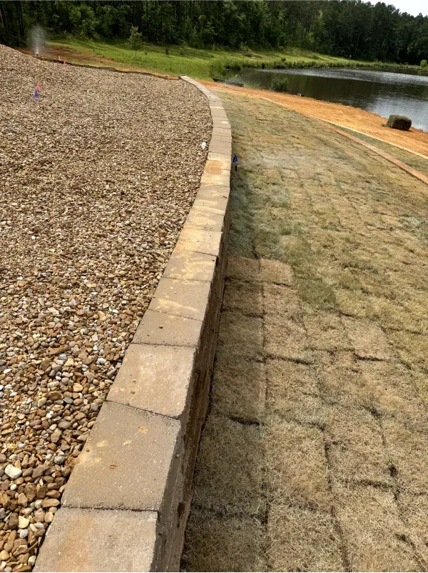 A brick walkway leading to a lake with gravel and grass.