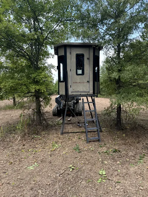 A small house with stairs is sitting in the middle of a field.