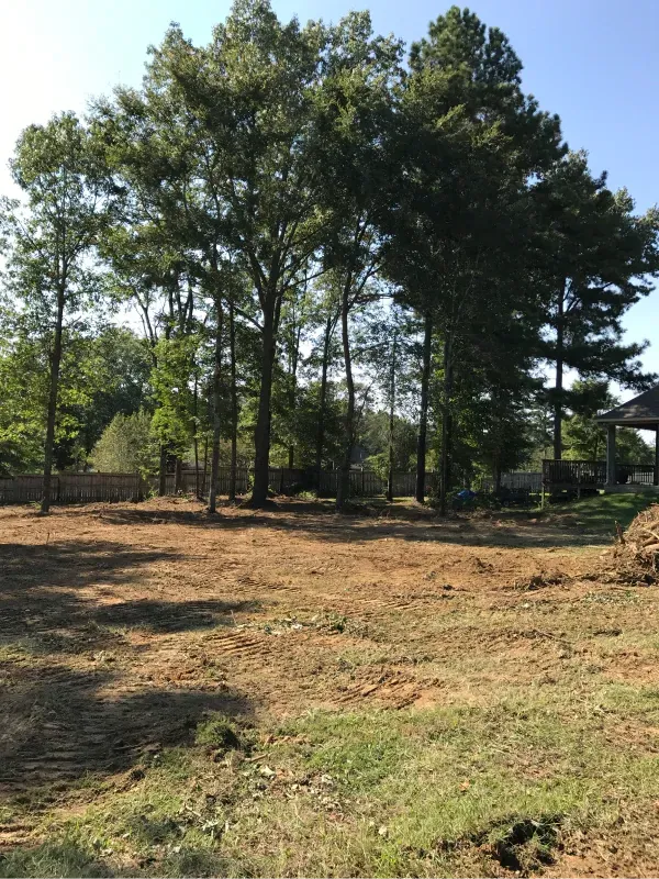 A dirt field with trees in the background and a house in the background