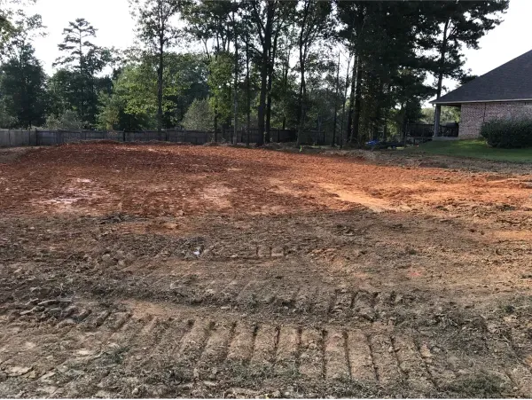 A dirt field with a house in the background and trees in the background.