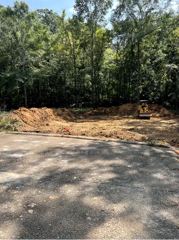 A bulldozer is sitting in the middle of a dirt field surrounded by trees.