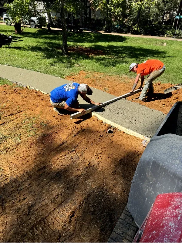 Two men are working on a sidewalk in a park.
