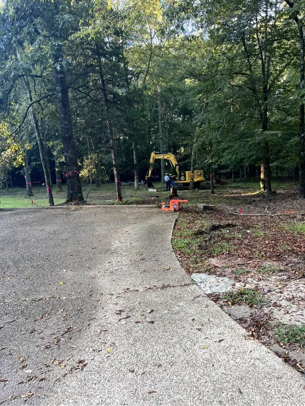 A yellow excavator is sitting on the side of a road in the woods.