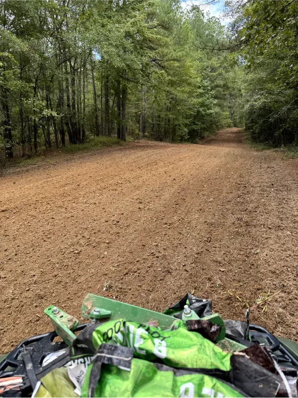 A person is riding an atv down a dirt road in the woods.