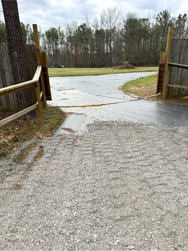 A concrete driveway with a wooden fence and trees in the background.