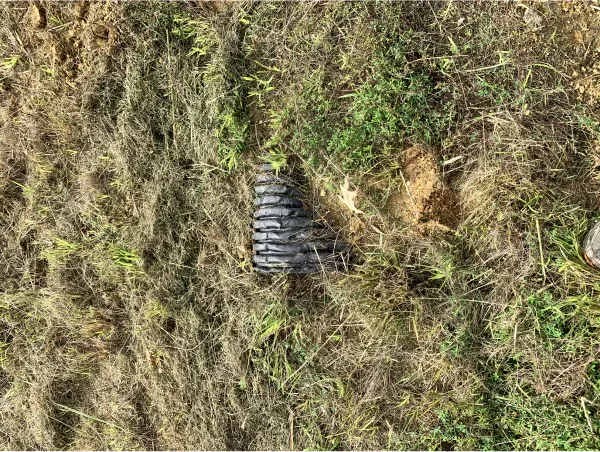 A person is standing in the grass next to a pipe.