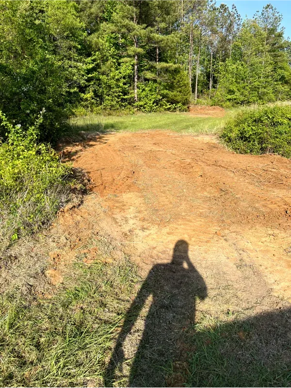 A shadow of a person is cast on a dirt road.