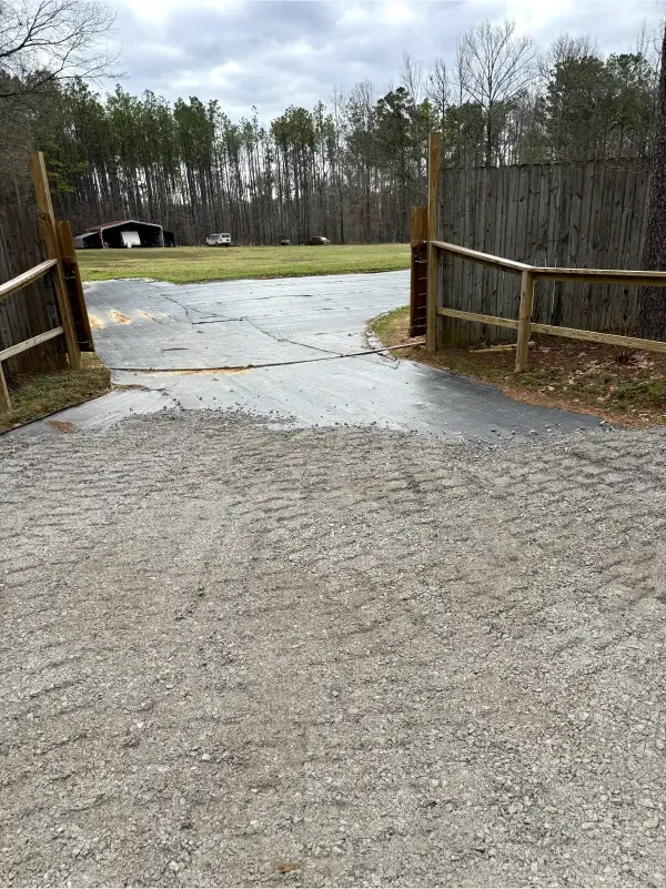 A dirt road with a wooden fence and a barn in the background.