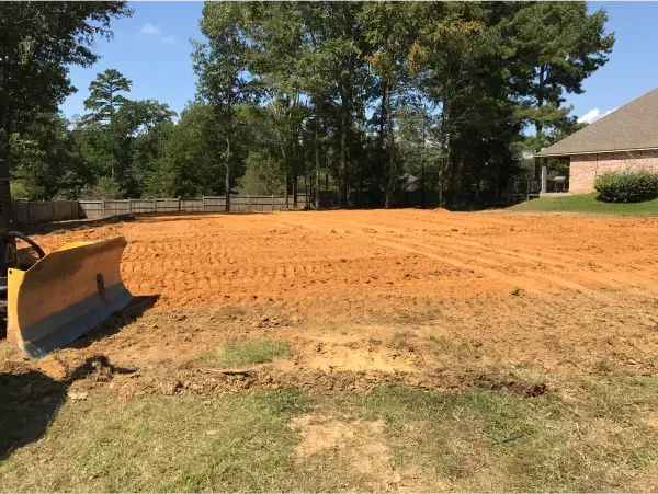 A bulldozer is sitting in the middle of a dirt field in front of a house.