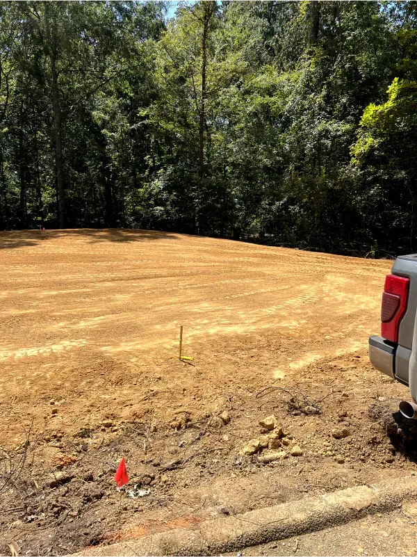 A truck is parked in a dirt field with trees in the background.