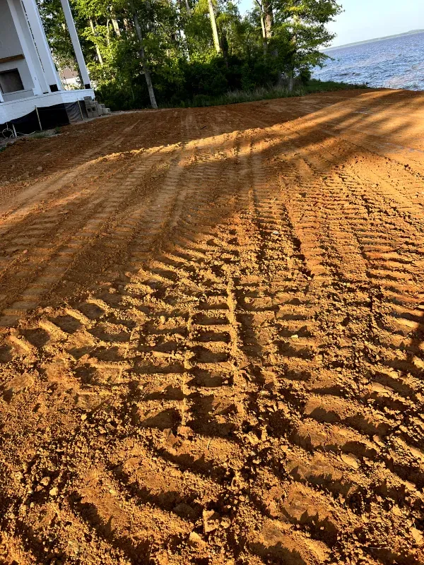 A dirt road with tire tracks in the dirt and a house in the background.