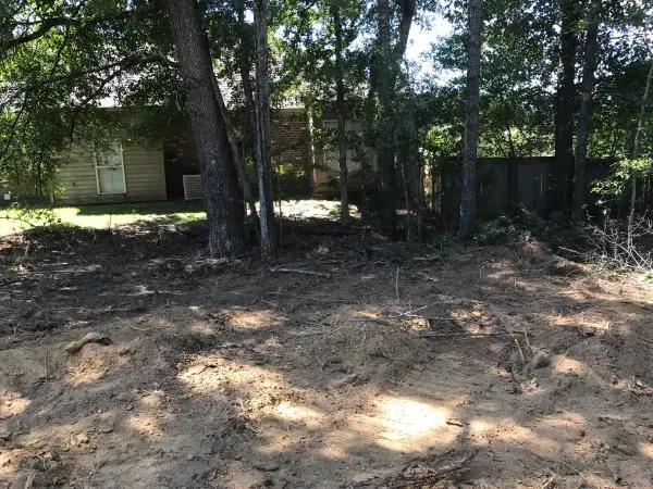 A dirt field with trees in the background and a house in the background.