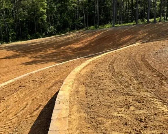 A dirt road with a concrete curb and trees in the background.