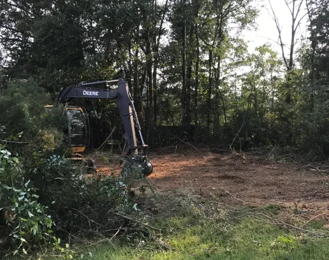A large excavator is sitting in the middle of a forest.