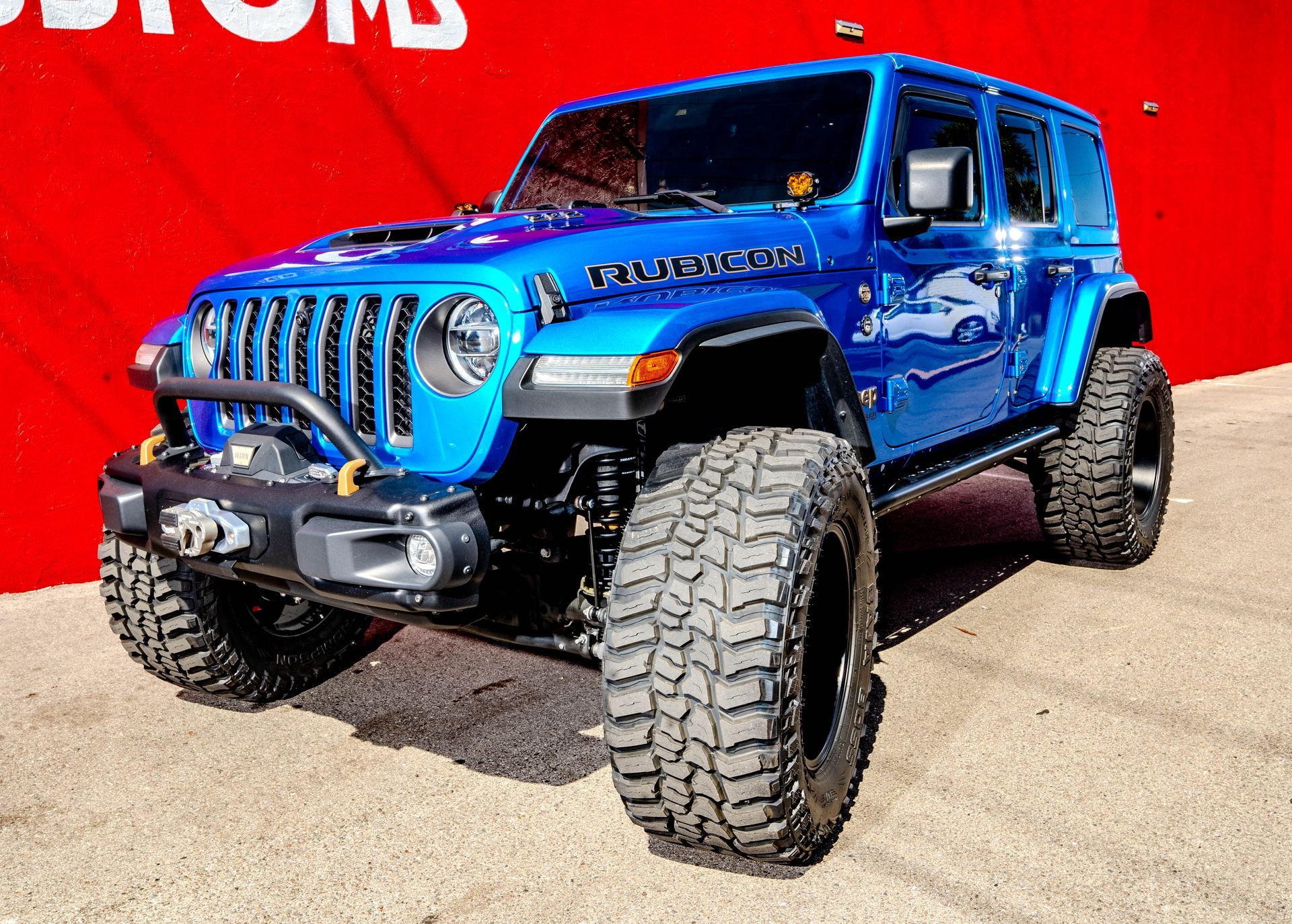A blue jeep wrangler is parked in front of a red wall.
