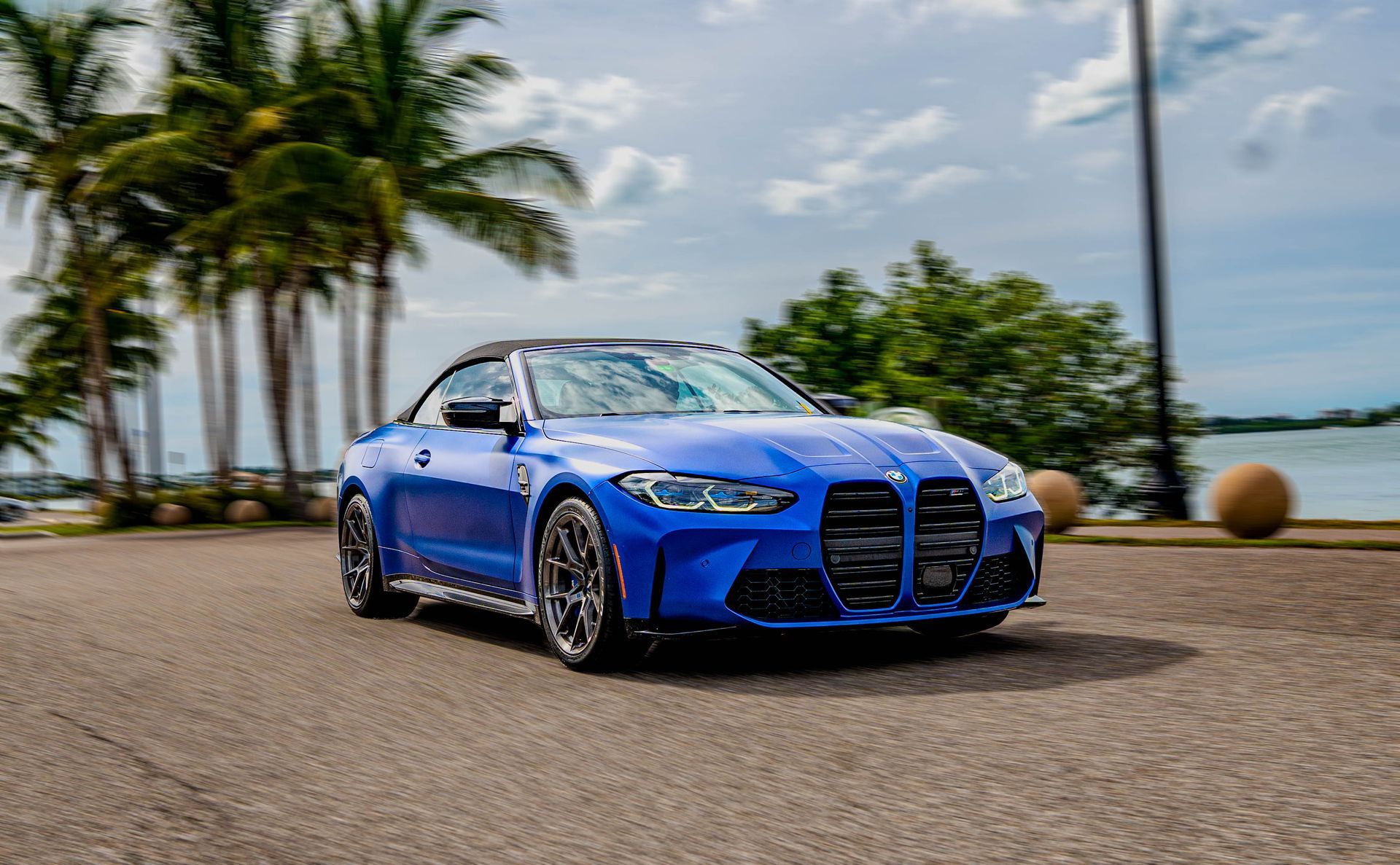A blue bmw m4 convertible is parked on the side of the road next to palm trees.