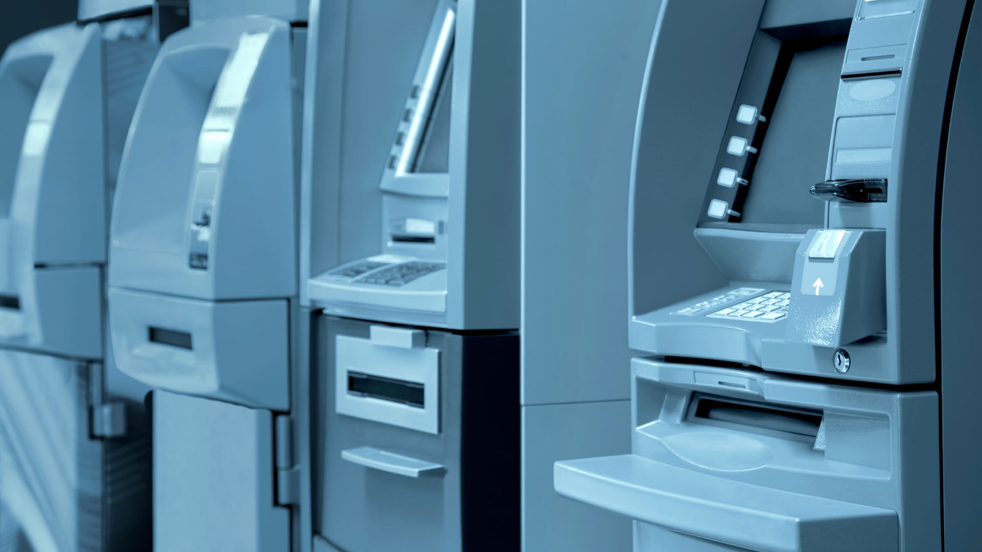 Row of ATMs in a bank lobby; pale blue color scheme.