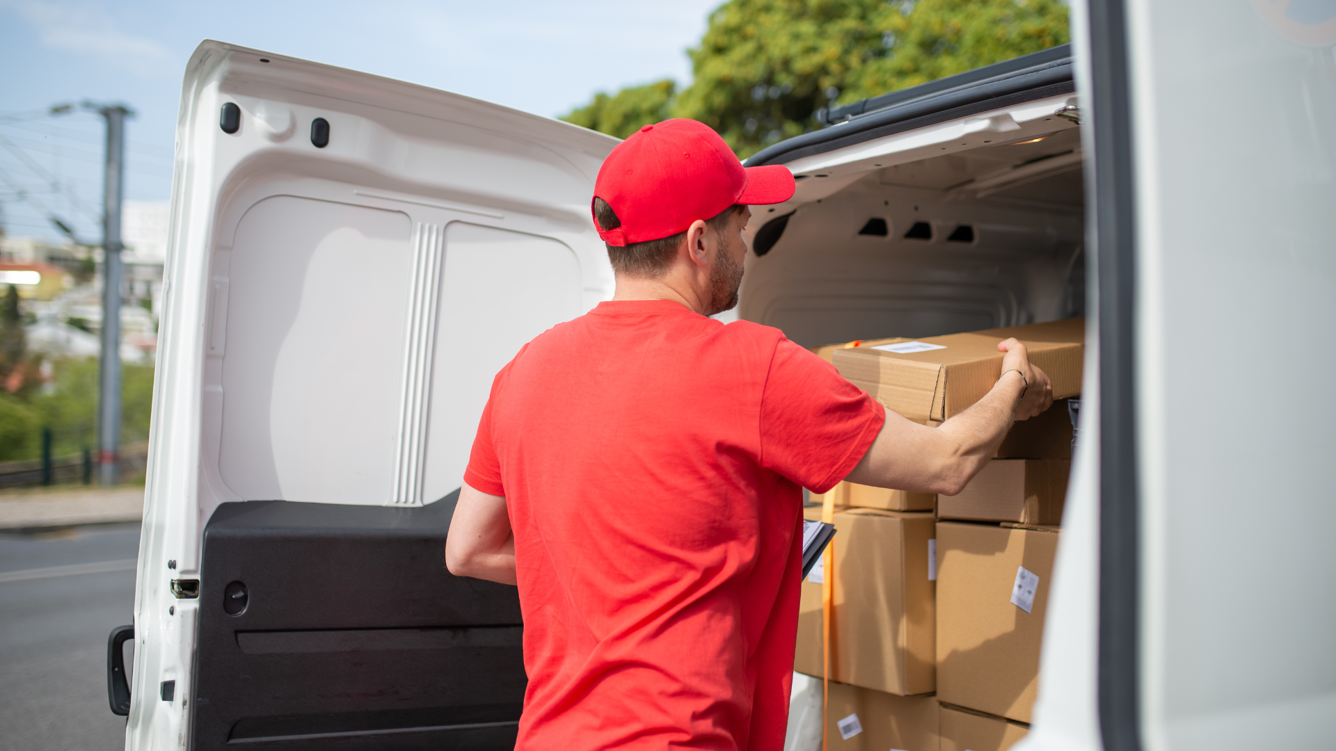 Delivery person in a red uniform loads packages into the back of a white delivery van.