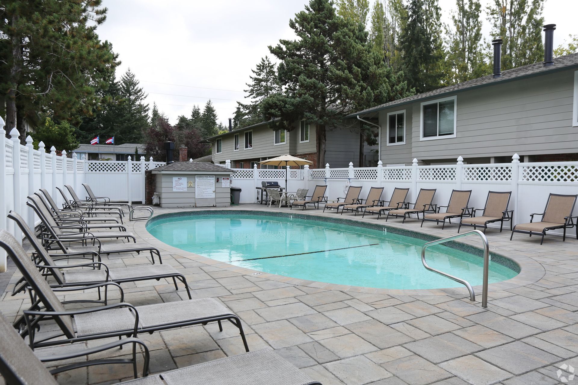 Swimming pool with lounge chairs, fenced in, near apartment buildings.