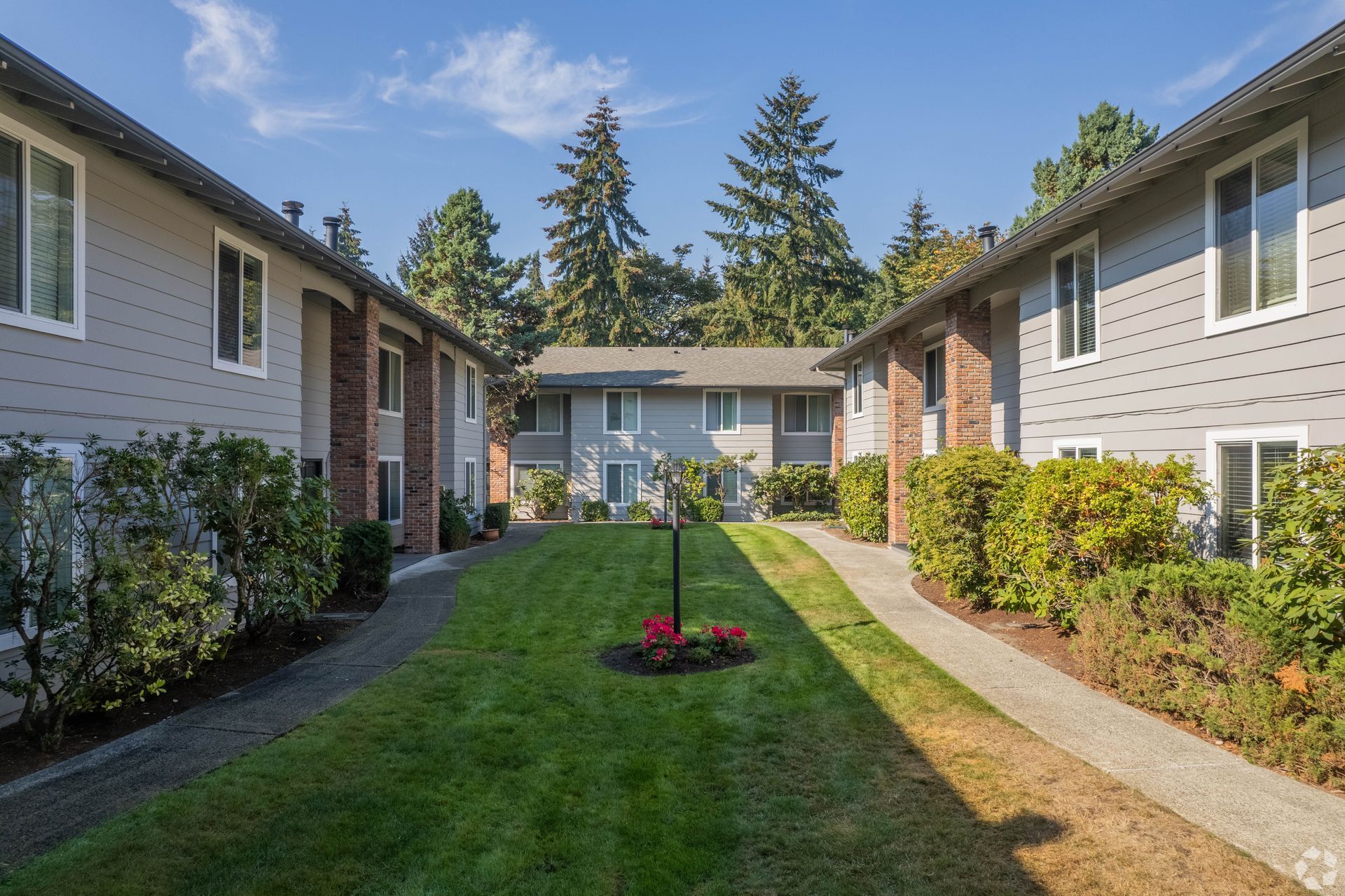 Apartment complex with grey siding, brick accents, and green lawn pathway.