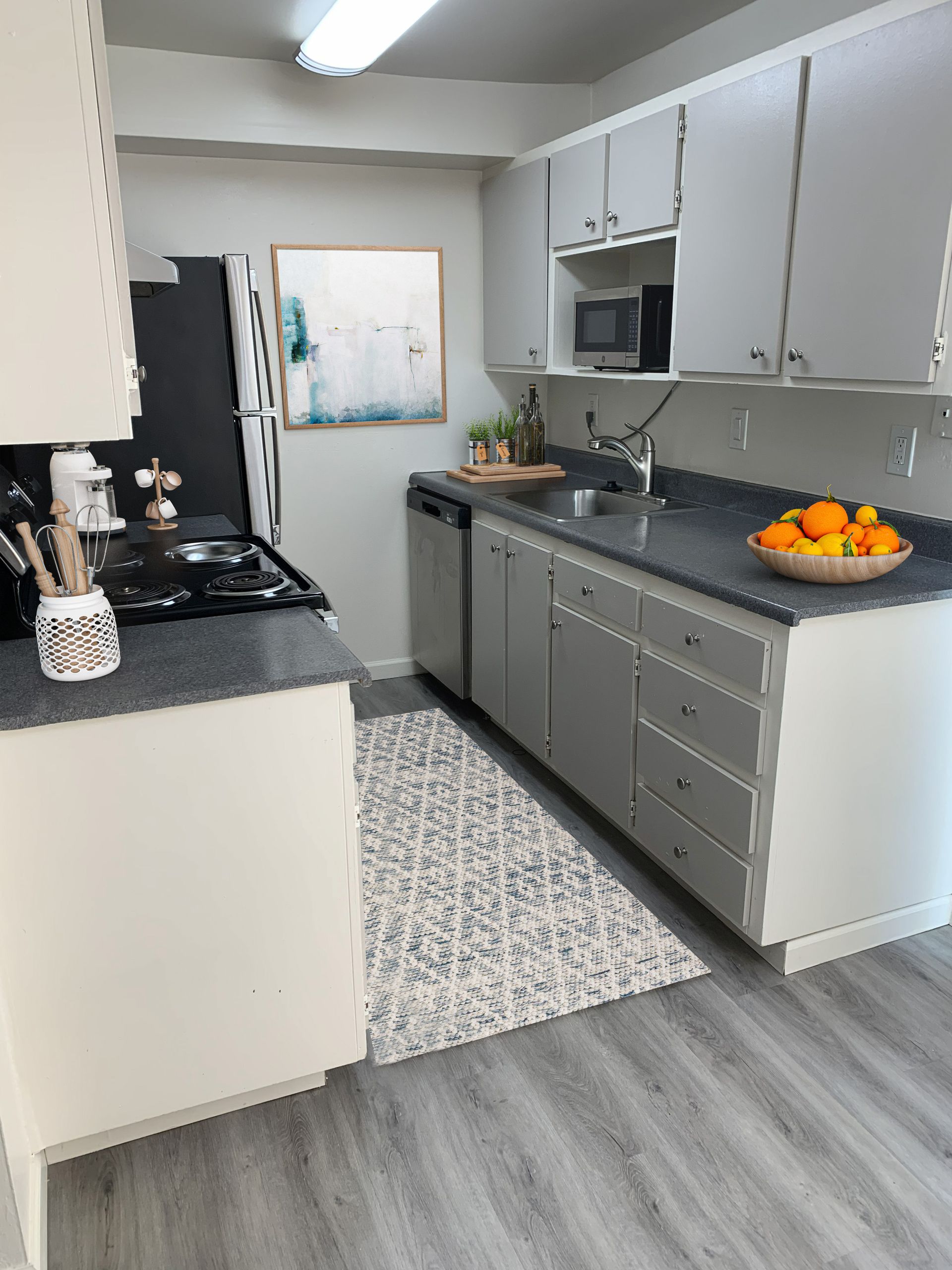 Kitchen with grey countertops, light cabinets, stainless appliances, and patterned rug.