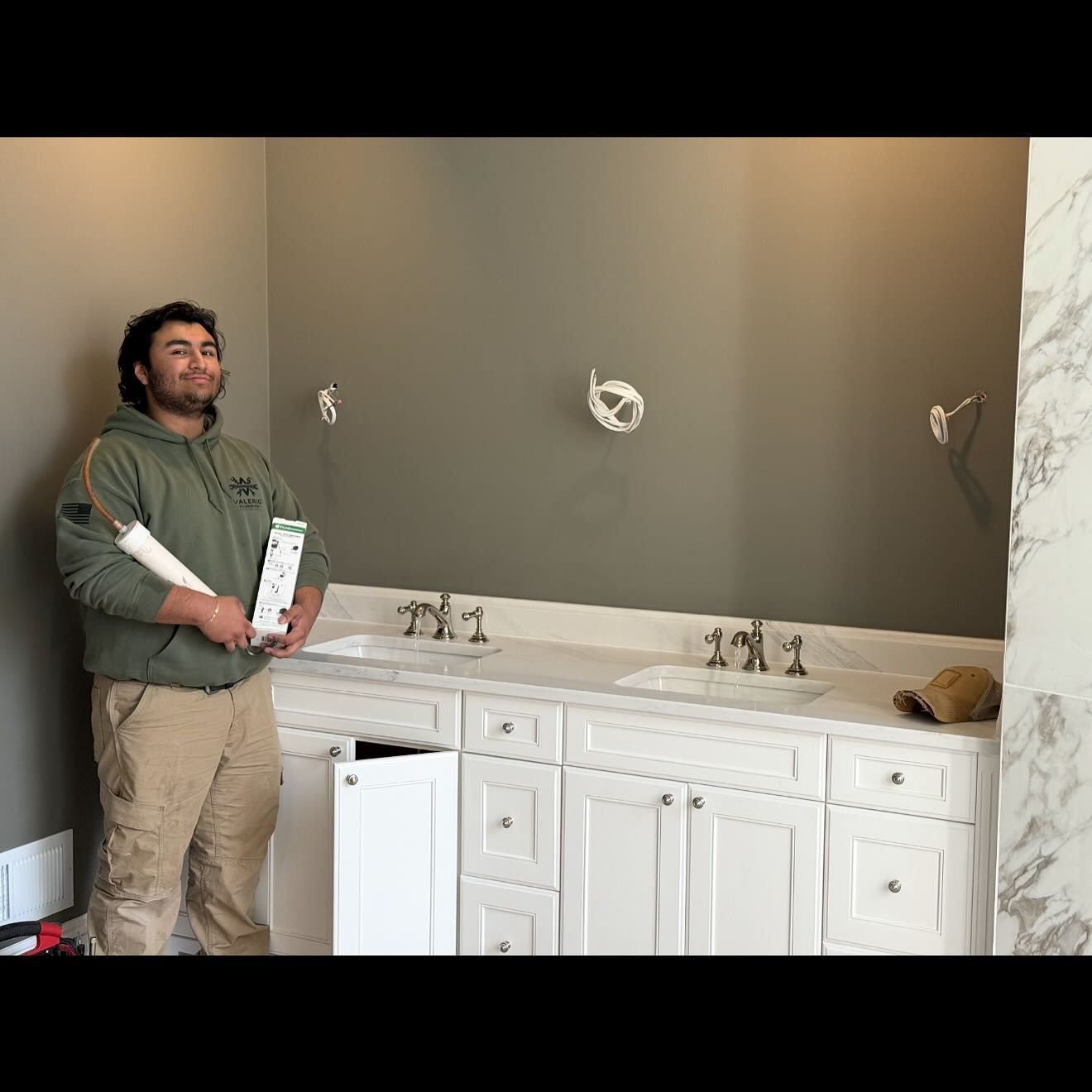 Man holding supplies in a bathroom under construction with a white vanity and gray walls.