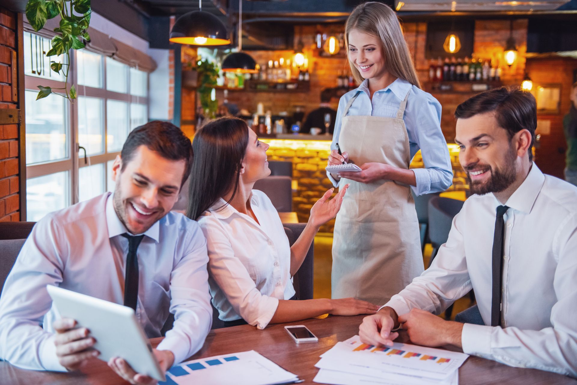 A group of people are sitting at a table in a restaurant looking at a tablet.