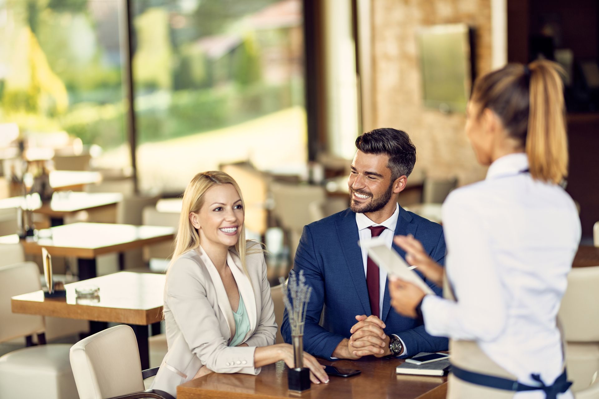 A man and woman are sitting at a table in a restaurant talking to a waitress.