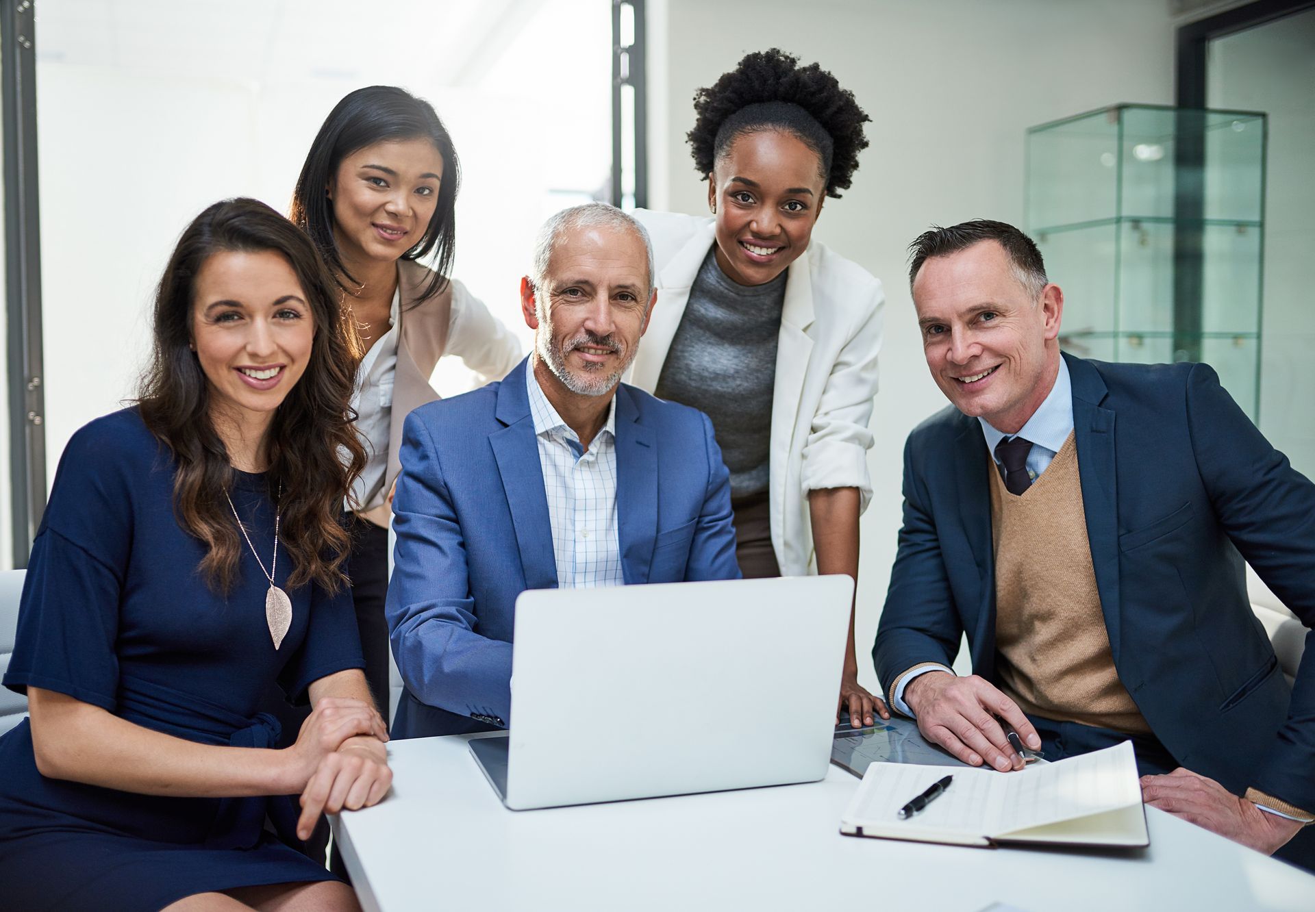 A group of business people are sitting around a table with a laptop computer.