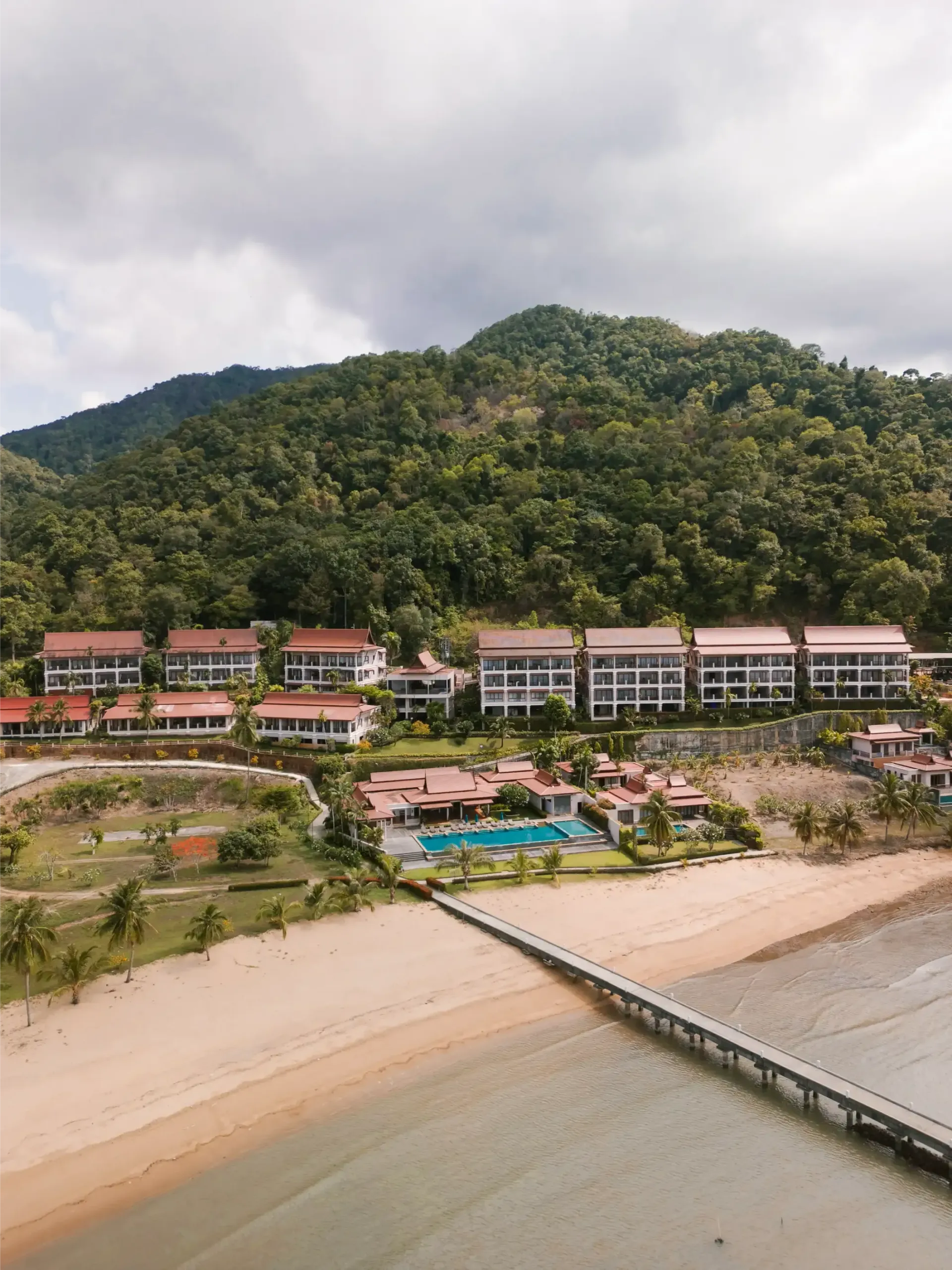An aerial view of a beach resort with a pier leading to it.