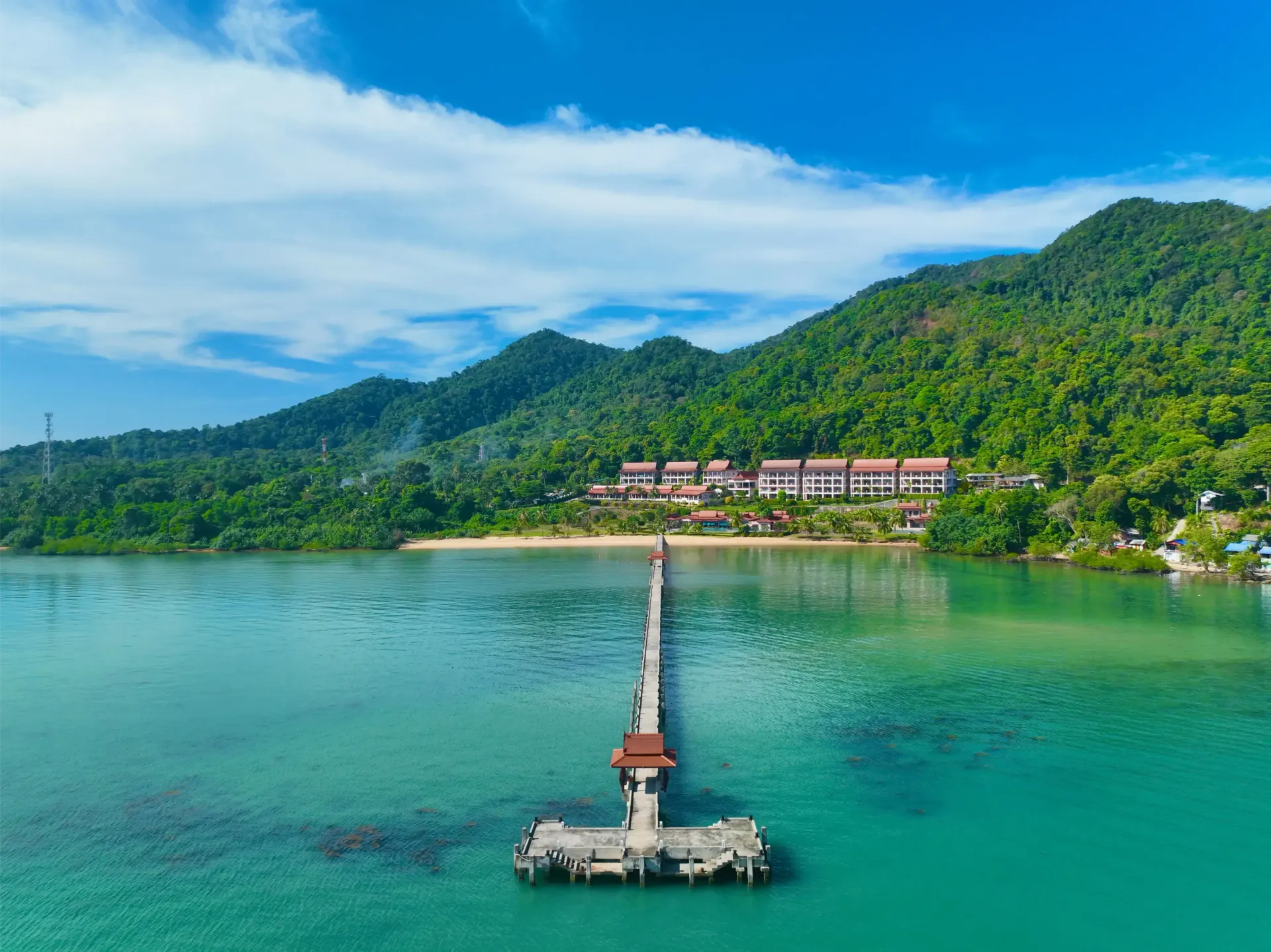 An aerial view of a dock leading to a beach with mountains in the background.