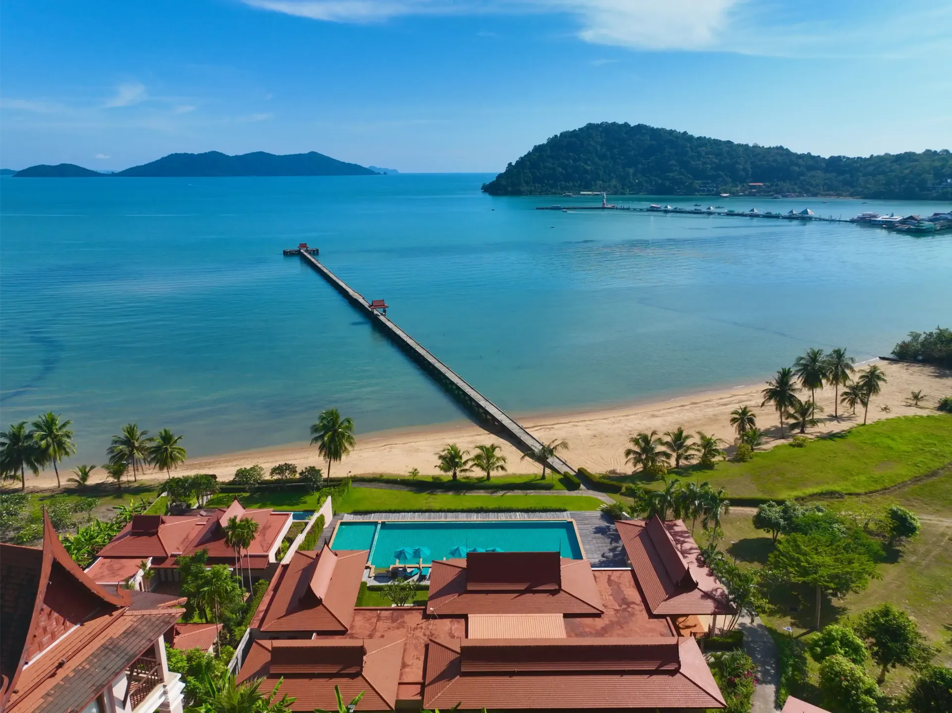 An aerial view of a resort with a swimming pool and a pier leading to the ocean.