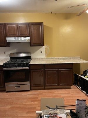 Kitchen with brown cabinets, gas stove, beige countertop, and golden wall. Flooring is wood.
