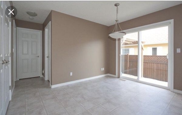Empty dining room with beige walls, sliding glass door, tiled floor, and a pendant light.